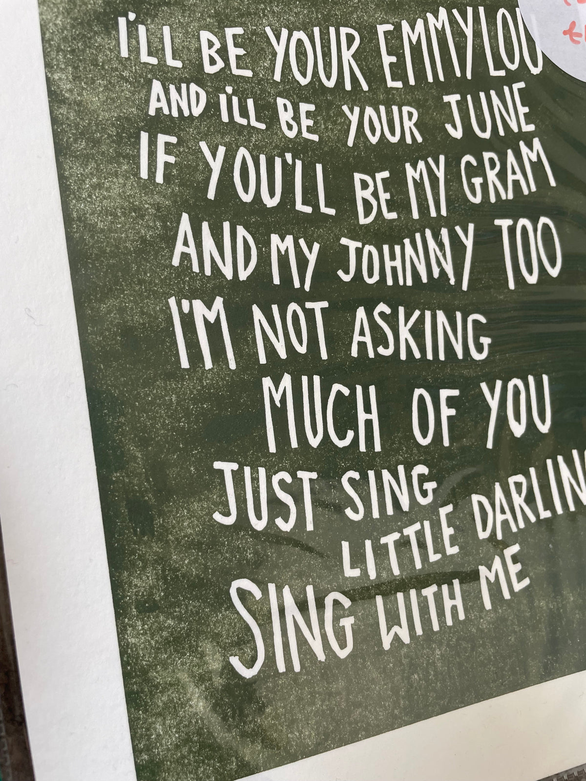A close-up of a typographic art print featuring white hand-lettered text over a dark olive green textured background, with a white border visible around the print.